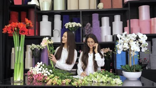 Two Female Florists Standing at a Table in Flower Workshop Holding a Bouquet of Flowers and Mixed