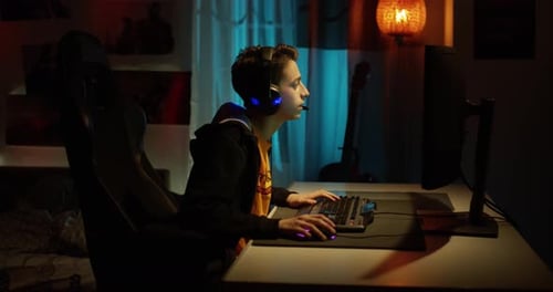 A teenage boy in headphones playing an online computer game, communicating with players, happy and e