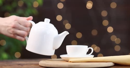 Woman pouring tasty green tea from teapot into cup at wooden table, closeup