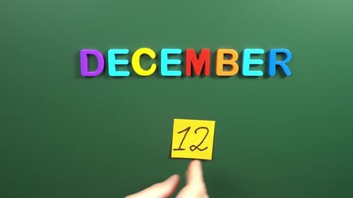 Hand sticking a sticker 12 December calendar day on school board. 12 date of December. Twelfth day
