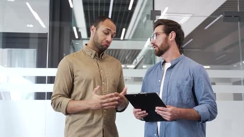 Two happy businessmen shaking hands after deal while talking standing in business office