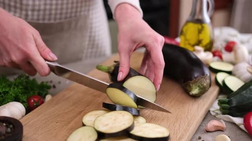 Frau schneidet frische Auberginen mit einem Messer auf einem Holzbrett