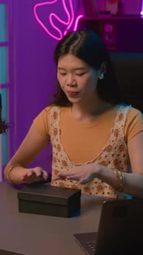 Vertical of Asian Female Presenter Unpacking Box with Cosmetics on Live Show