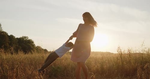 Happy Mother Spinning Her Son Holding Hands in a Golden Field at Sunset