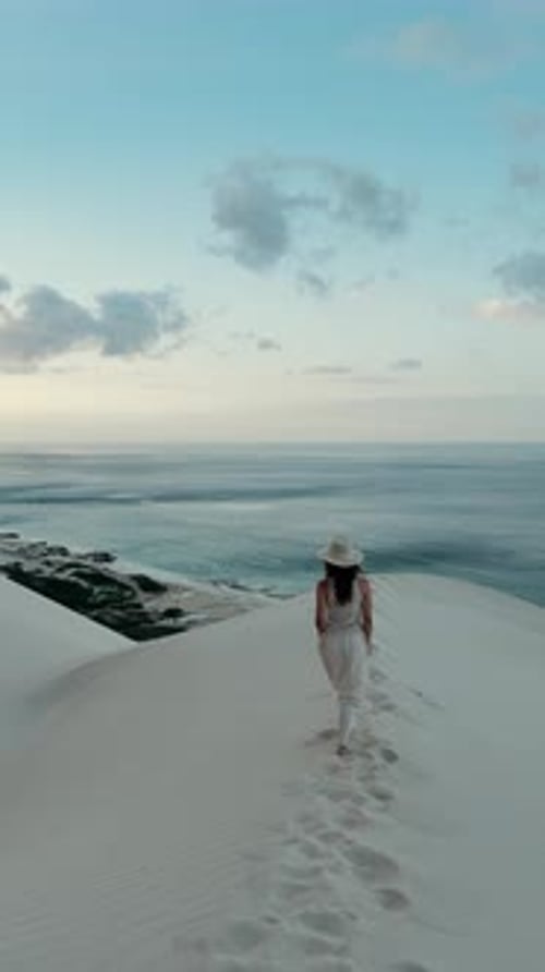 A Woman is Gracefully Walking Along the Beautiful Scenic Beach Dunes During a Stunning Sunset