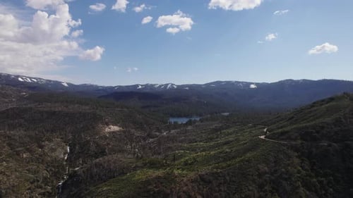 Aerial panoramic view of mountain landscape on sunny day. Wooden hills and slopes and water reservoi