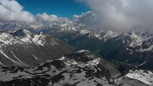 Air flight through mountain clouds over beautiful snow-capped peaks of mountains and glaciers.