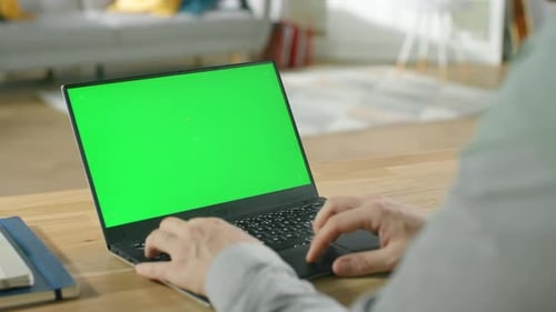 Professional Freelancer Works on a Laptop with Green Mock-up Screen while Sitting at the Desk in Hi