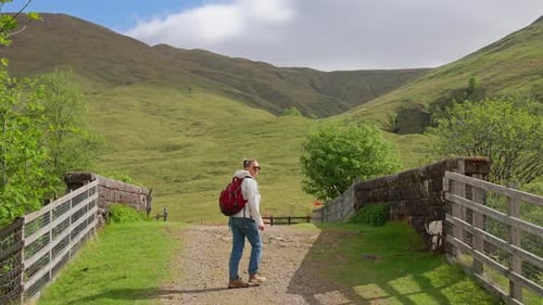Woman walking and turns around viewing majestic green Scottish rolling hills on West Highland Way