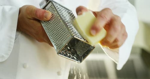 An experienced chef in a professional kitchen Grating Parmesan to prepare a sauce or to put on ita