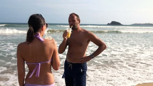 Young couple enjoying cocktails on a sunny beach in super slow motion