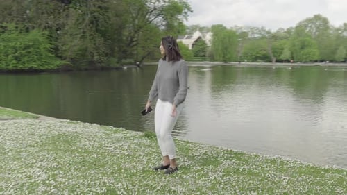 Photographer captures young woman enjoying music by a tranquil pond in the park