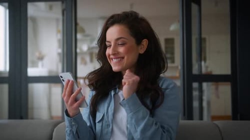 Excited Woman Celebrates Success on Mobile Phone Indoors