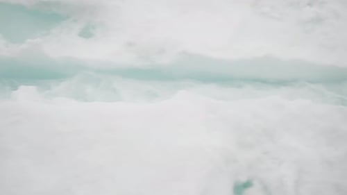 Zerbrochenes Meereis mit sichtbaren türkisfarbenen Schmelzwassernähten und treibenden Eisschollen geht über in weiches