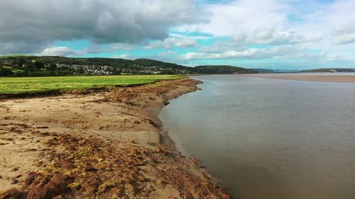 Low aerial shot along a sloped Sandy bank, on the shoreline, bright sunny day.