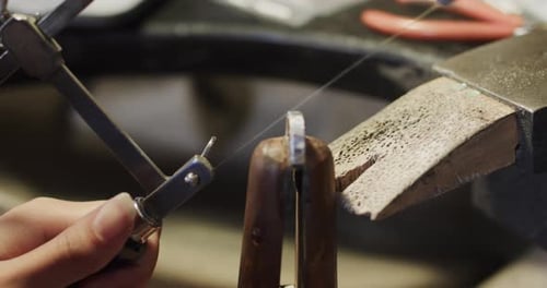Caucasian female worker shaping jewellery with saw in studio in slow motion
