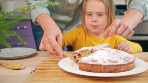 Child Receives Cake Slice from Adult in Kitchen