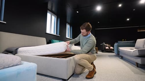 Young Handsome Man Examining Orthopedic Mattress at Furniture Store