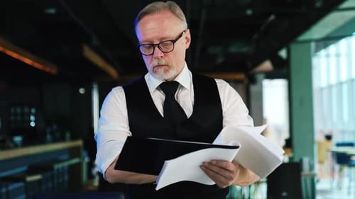 Businessman stands in office holding documents in hands. Boss checking some papers at work.