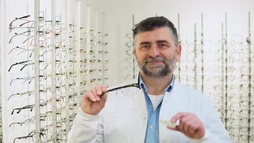 Oftalmólogo senior seguro de sí mismo sostiene lentes de contacto y anteojos en las manos