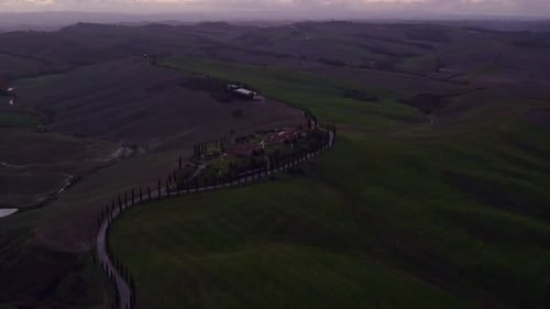 Aerial view of tranquil villa and cypress-lined hills at sunset, Italy.
