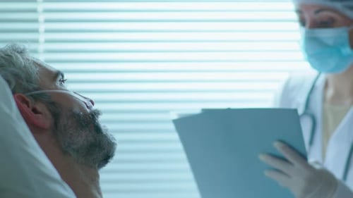 Patient and Female Doctor in Protective Uniform Talking in Hospital Ward