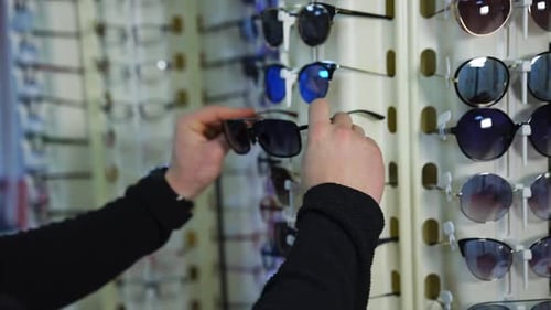 Fashionable sunglasses on stand at optics. Man testing new glasses in the shop.