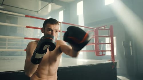 Young Boxer with Bare Muscular Torso Performing Shadow Boxing in Gym