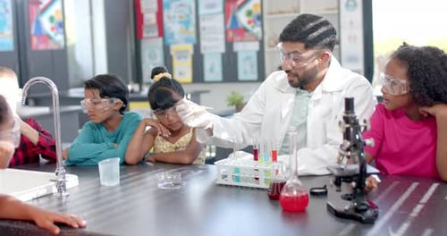 In a school laboratory, a biracial teacher demonstrates a science experiment