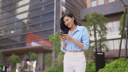 Portrait of Asian businesswoman using smartphone while standing in city.