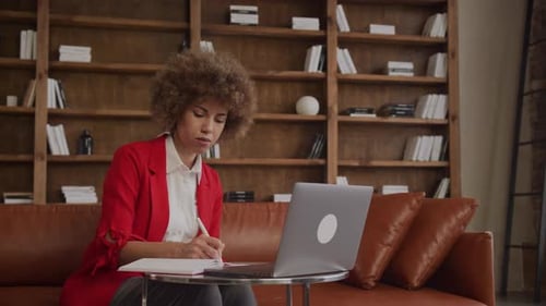 Woman Works on Laptop and Writes in Notebook
