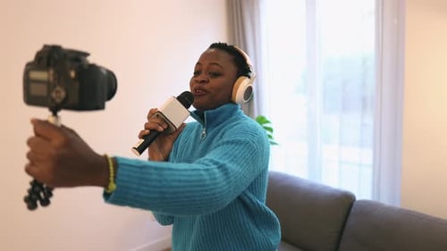 African american woman recording music tutorial with camera at home looking positive and happy stand