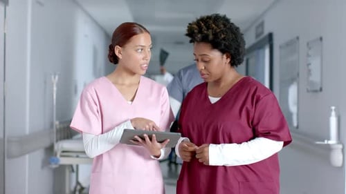 Women Discussing Tablet in Hospital Hallway