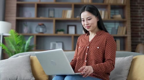 Young Woman Works on Laptop at Home on Couch