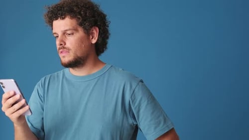 Thoughtful man with phone in his hands c mockup space in studio on blue background