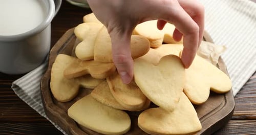 Woman taking tasty heart shaped butter cookie from board at wooden table, closeup