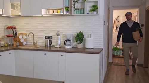 Young man arrives home from the market carrying fresh groceries and placing them on the kitchen coun