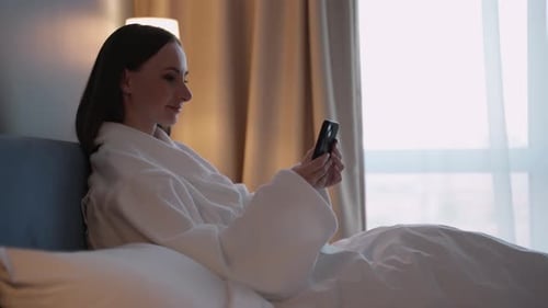 Woman in Robe Using Phone in Bed