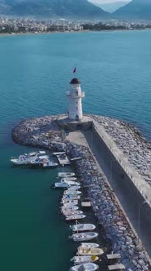 Vertical Video of a Tall White Lighthouse in the Port Captured From Above Overlooking the Ocean and