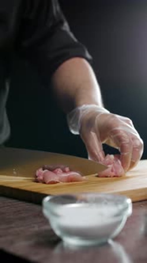 Mit behandschuhten Händen das Hähnchenfilet vorsichtig mit einem scharfen Küchenmesser abschneiden.