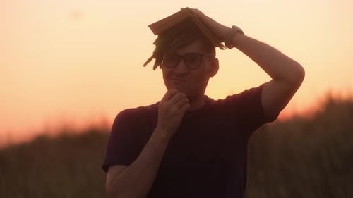 Jeune homme perplexe dans des lunettes tenant un livre au-dessus de la tête alors que le toit grattant le menton lève son index