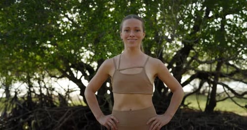 Portrait of Positive Sportive Woman in Activewear Holds Hands on Hips in Park