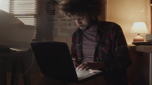Middle Eastern Nerd with Messy Curly Hair Typing on Old Laptop