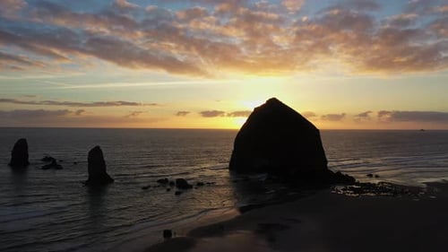 Majestic aerial sunset shot of sea stacks and boulder in ocean on the beach of California.