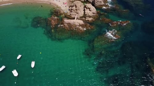 Flying above the rocky coastline, next to a beach and a port of yachts on the Mediterranean Sea