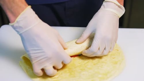 Fleisch- und Käse-Pita mit Gemüse kochen. Hände in Latexhandschuhen rollen eine Pita-Rolle zusammen.