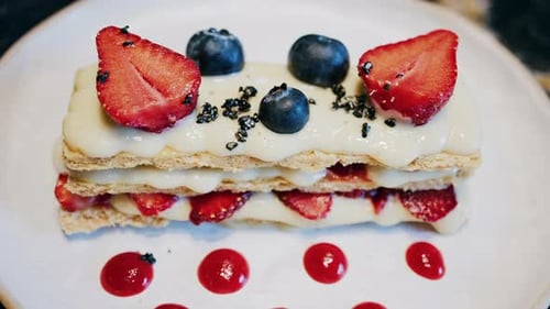 Close up of a Napoleon cake with strawberries and blueberries on a white plate at a cafe
