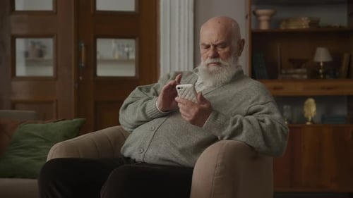 Senior Man Using Smartphone While Sitting Indoors
