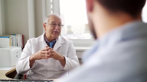 Senior doctor talks to young male patient about health problems at hospital
