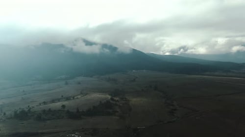 Drone shot of a field and мountain with cloudy sky